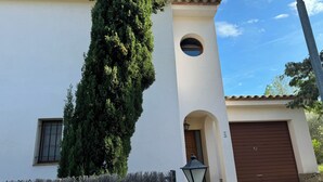 A building with a white facade, a brown garage door, and a tall green tree in front.