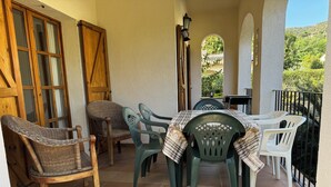 A covered patio with a table and chairs, a wooden door, and a view of greenery.