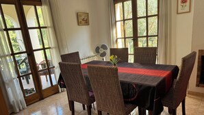 A dining area with a table set for four, surrounded by wicker chairs, a fan, and a vase with flowers.