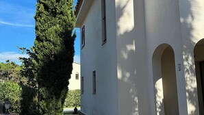 A building with a stone-paved entrance, a tall tree, and a black metal railing.