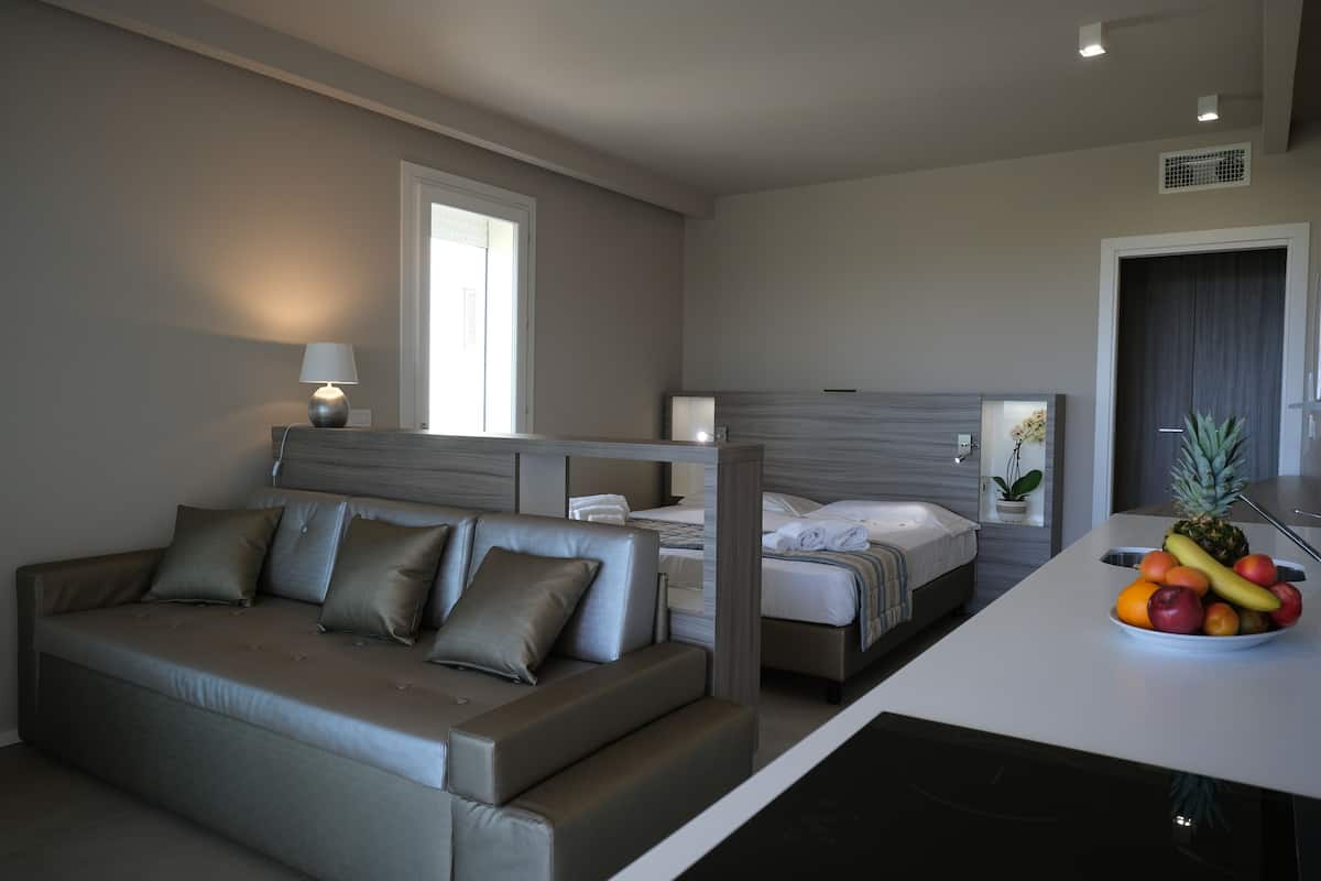 Ein modernes Hotelzimmer mit einer Couch, einem Bett, einer kleinen Essecke und einer Obstschale.