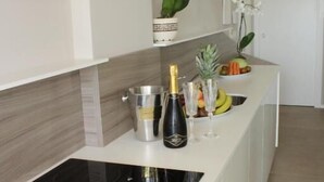 A modern kitchen with a built-in stove, a white countertop, and a small island with a fruit bowl and decorative items. - AlMar Apartments by Alma di Alghero (Alghero)