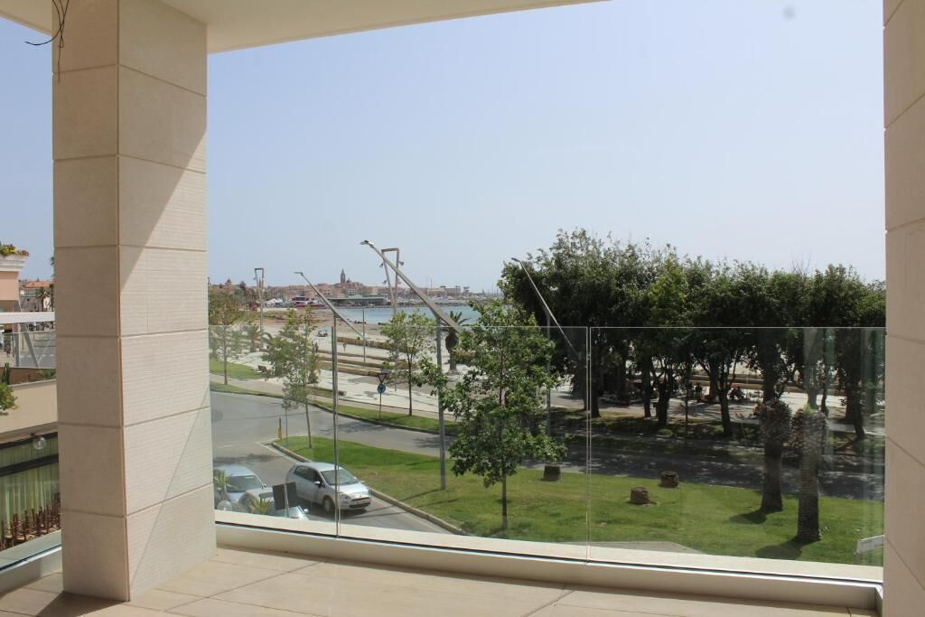 A balcony with a view of a park, a road, and distant buildings.