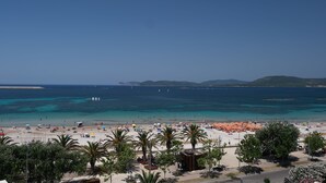 A beach with palm trees, umbrellas, and a clear blue sea. - AlMar Apartments by Alma di Alghero (Alghero)