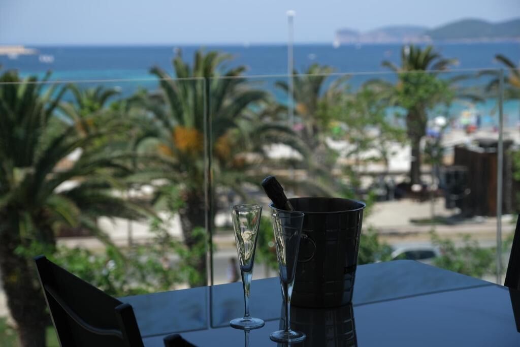 A table with a champagne flute and a bottle, overlooking a beach with palm trees and the sea.
