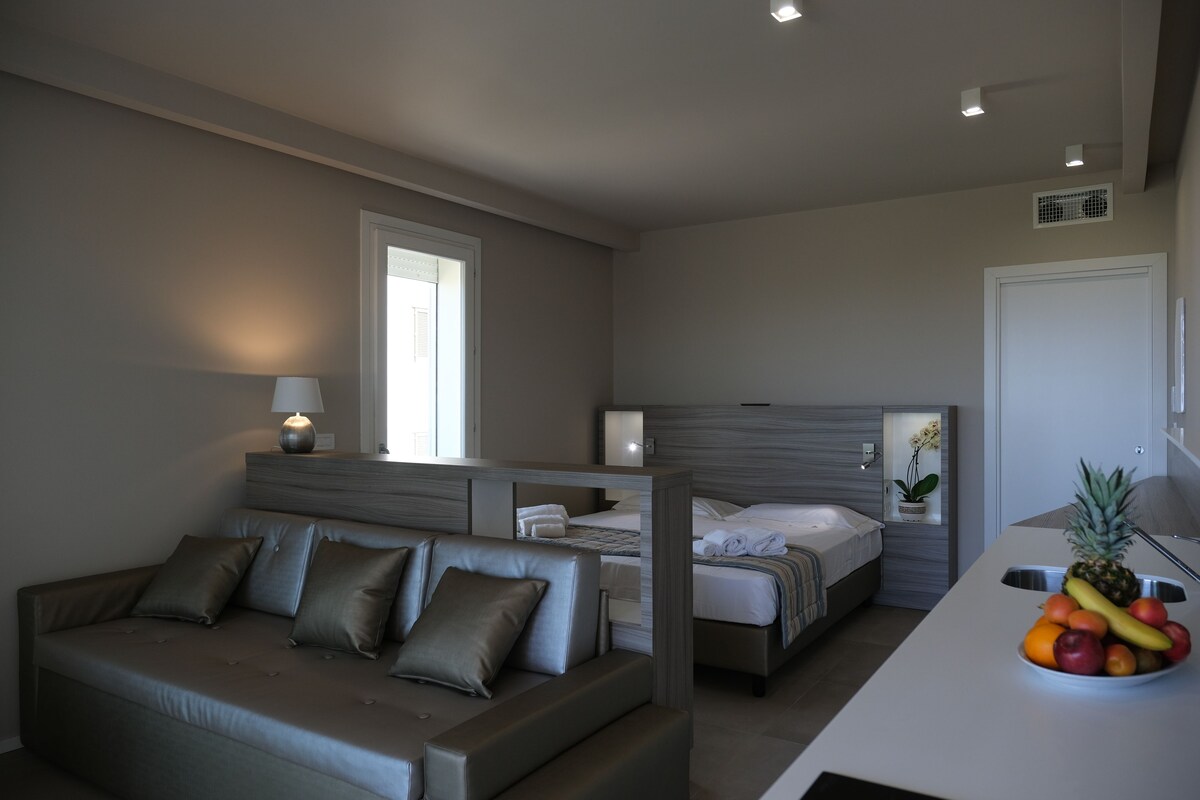 A modern bedroom with a sofa, a bed, and a fruit bowl on a counter.
