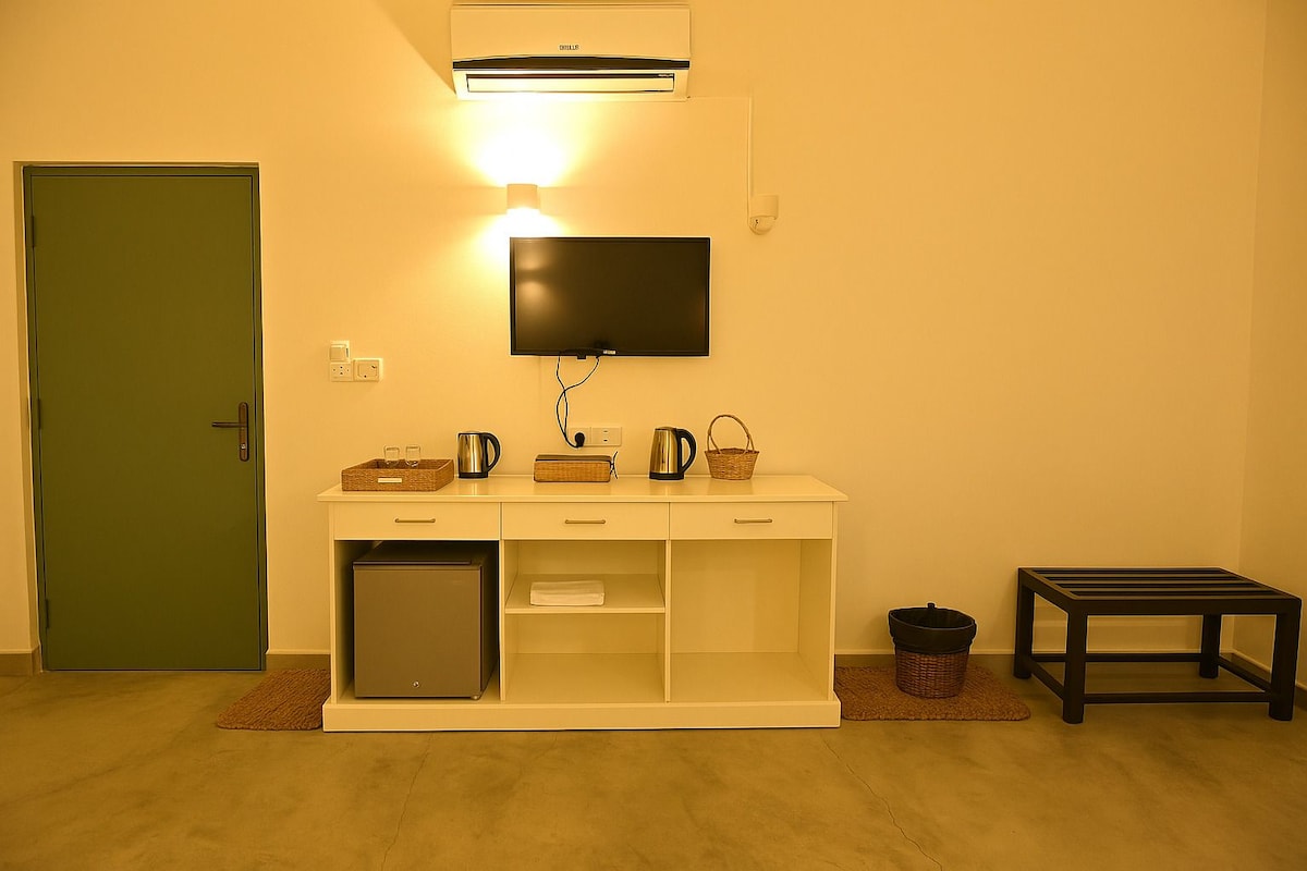 A compact living space with a kitchenette, a flat-screen TV mounted above a white console table, a green door, and a small black table.