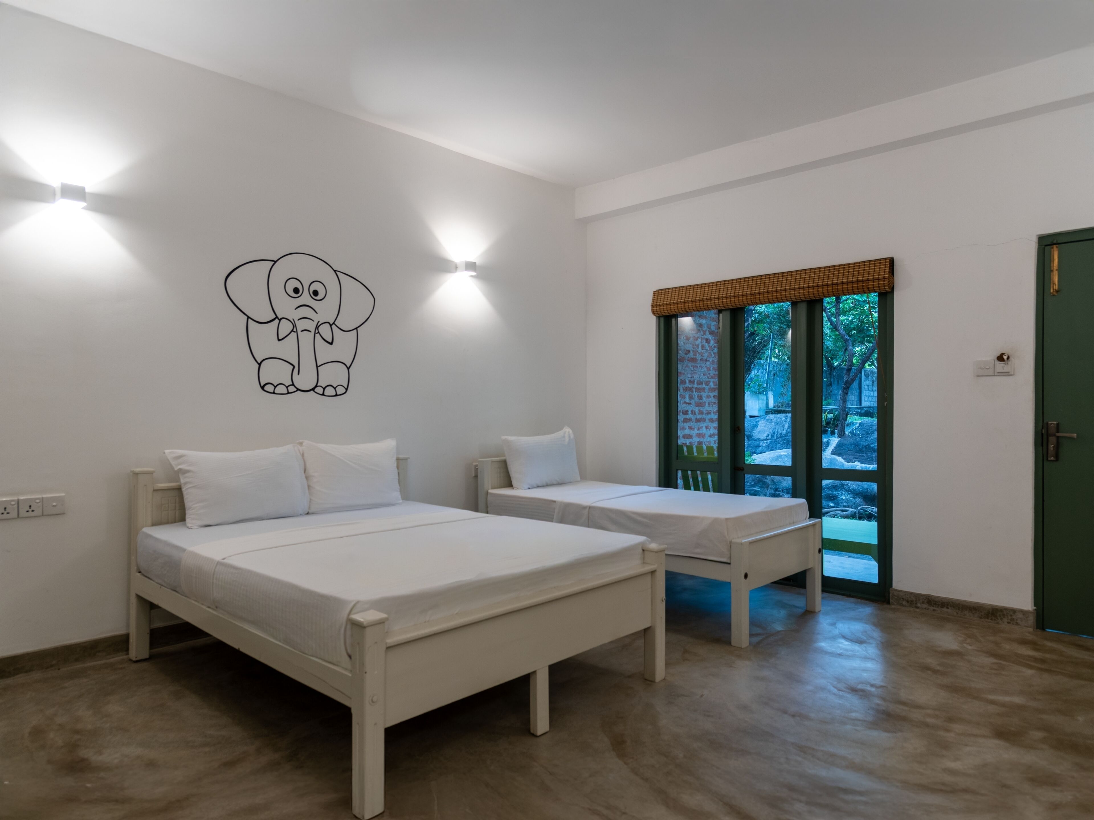 A room with two beds, a wall-mounted elephant decal, and a window with a view of greenery.