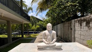 A meditative statue on a platform with a small altar in front. - Moi Dambulla by DBI (Sigiriya)