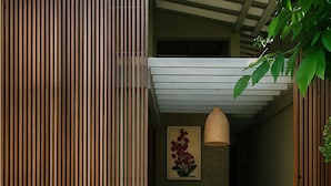 A modern interior with a wooden slatted wall, a wicker hanging light fixture, a cushioned chair, and a framed artwork on the wall. - Moi Dambulla by DBI (Sigiriya)