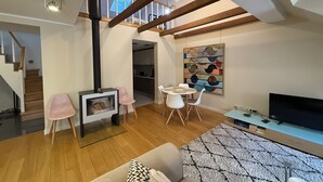 A spacious living room with a high ceiling, wooden beams, a fireplace, a dining area with chairs, a television, and a kitchen in the background. - Stylish Duplex in Tallinn’s Old Town with Fast WiFi  (Tallinn)