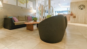 A modern lobby with a sofa, a round wicker chair, a coffee table, and wall art. - A Hotel Joo Chiat (Singapore)