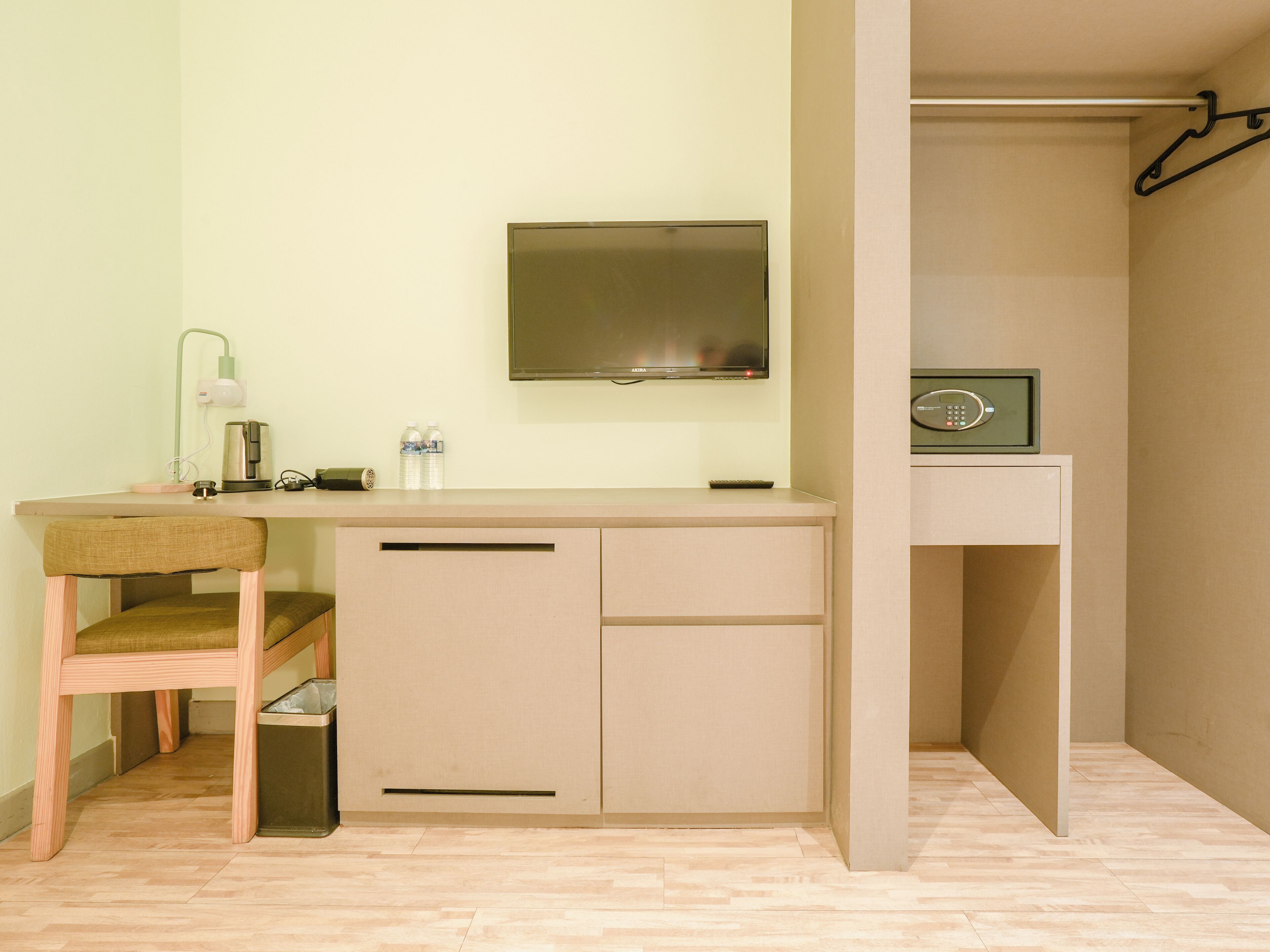 A small, modern room with a kitchenette, a TV mounted on the wall, and a coat rack.