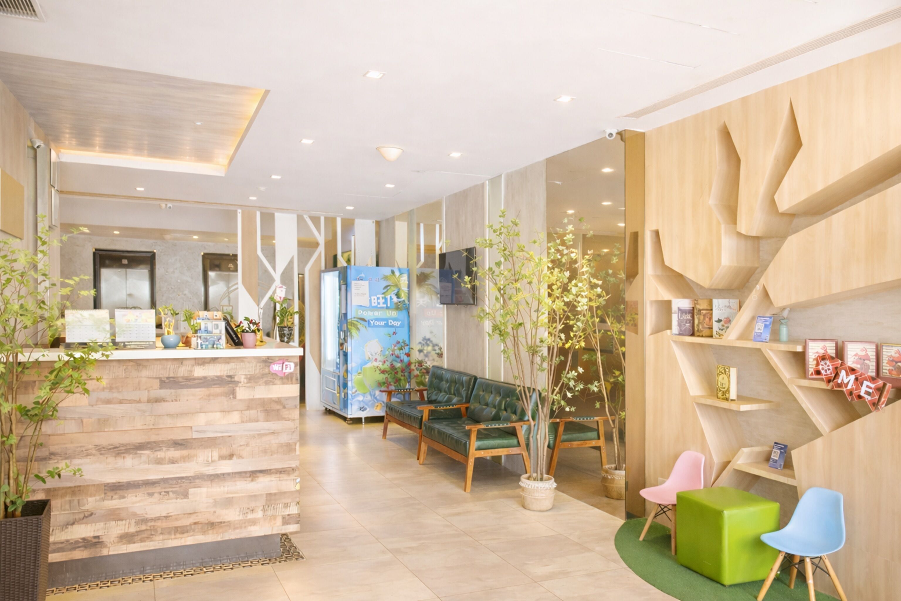 Un área de recepción con un mostrador de madera, sillas verdes y rosas, un sofá verde y un televisor montado en la pared.