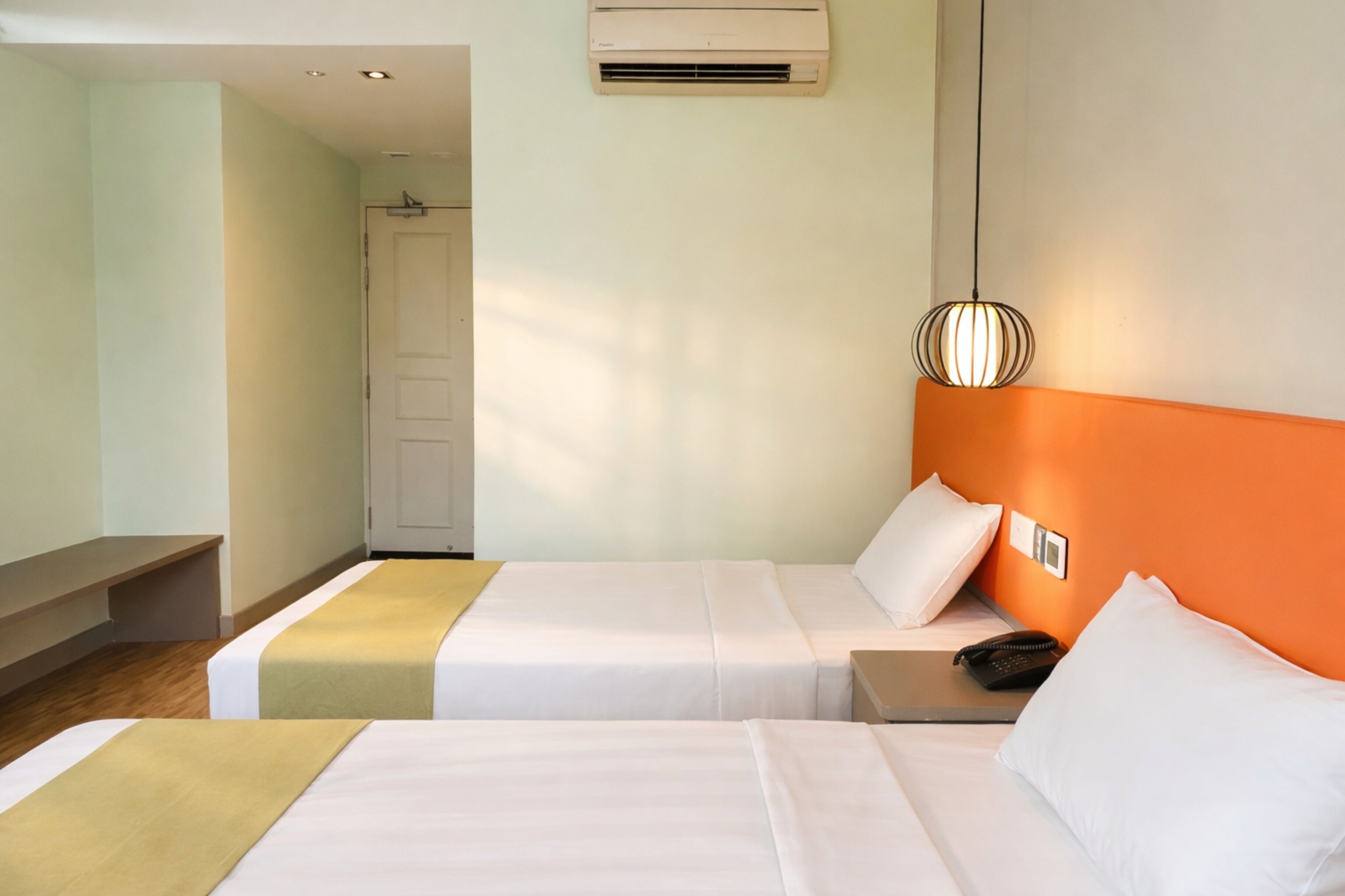 Ein Hotelzimmer mit zwei Betten, einem Nachttisch mit Telefon, einer Klimaanlage und einer wandmontierten Lampe.