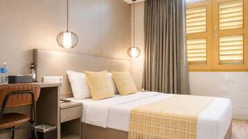 A hotel room with a bed, bedside table, chair, and a window with curtains.
