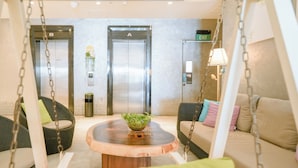A lobby with two elevators, a wooden table with a bowl of greens, and seating areas with cushions. - A Hotel Joo Chiat (Singapore)