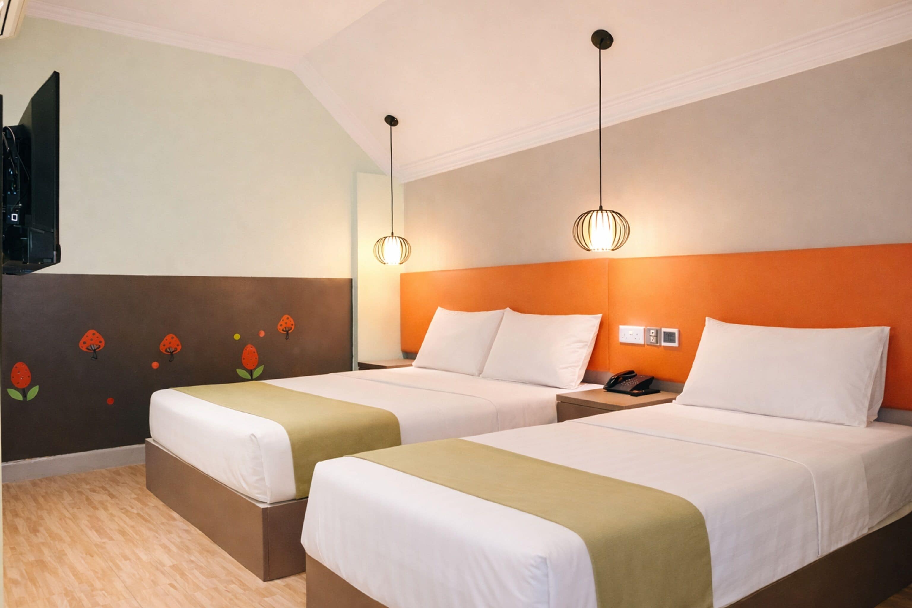 A hotel room with two beds, a television, and a wall with fruit decals.
