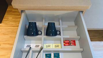 A drawer with two dark blue mugs, two white sugar packets, two non-dairy creamers, a Nescafé Classic coffee box, and two packets of Ceylon tea.