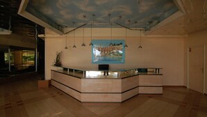 Un área de recepción con mostrador curvo, iluminación colgante, un cuadro grande y suelo de baldosas.