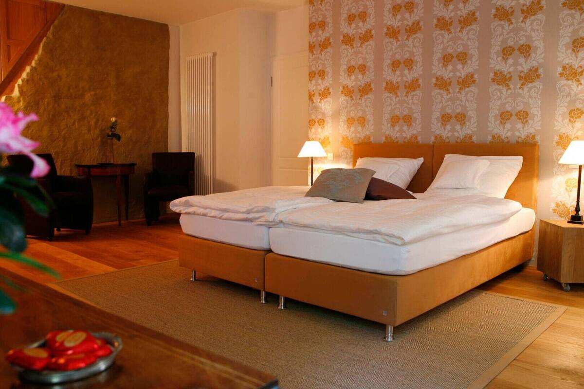 A double bed with two bedside tables, each with a lamp, in a room with wooden flooring and a floral wallpaper pattern.