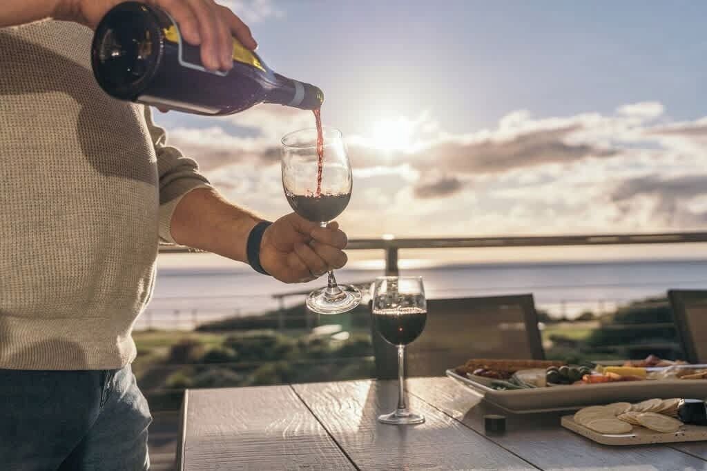 A person pouring wine into a glass, a table with food, and a scenic view.