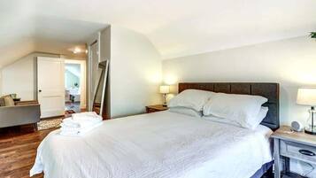 Un lit bien fait, avec du linge de lit blanc, une table de chevet avec une lampe et une petite table en bois à côté du lit.