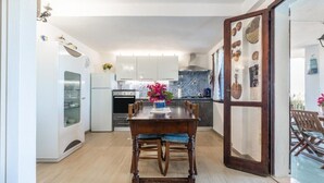 A modern kitchen with white cabinets, a wooden dining table, and a blue tiled backsplash. - Casa Ines Costa Rei, Sea View, 3 min from the Beach. (Costa Rei)