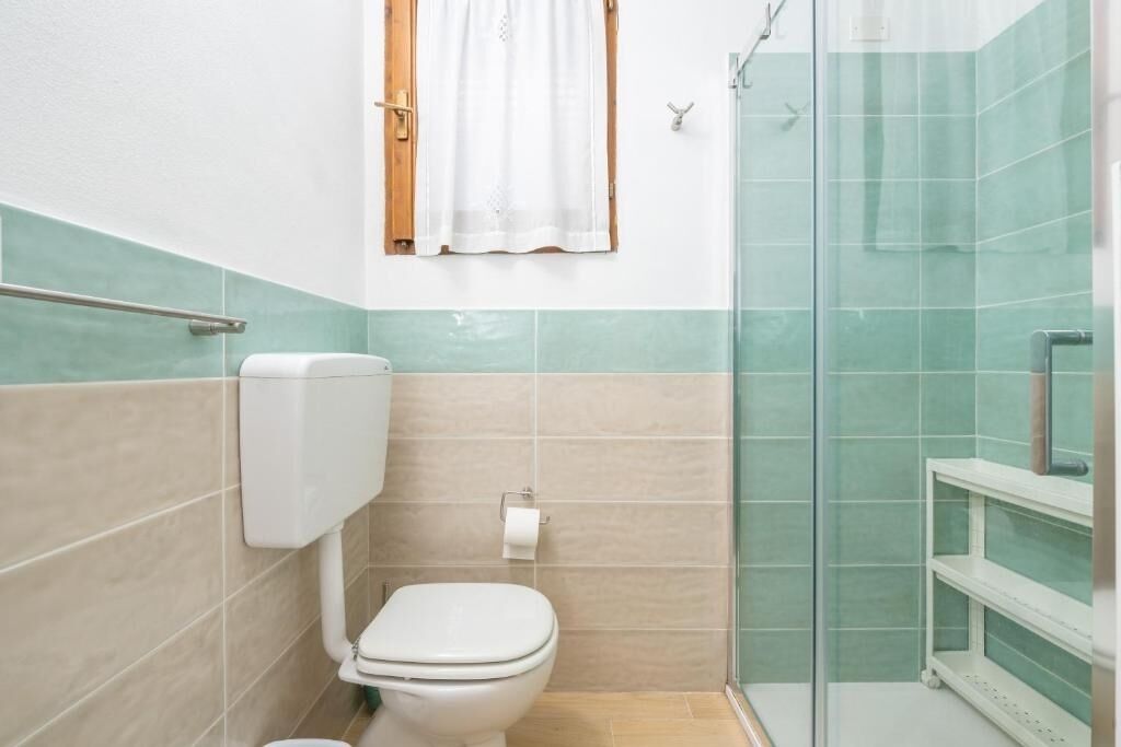 A small bathroom with a toilet, a glass shower enclosure, and a white towel hanging on the wall.