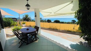 A covered patio with a round table and chairs, a view of the sea, and a yellow fence. - Casa Ines Costa Rei, Sea View, 3 min from the Beach. (Costa Rei)
