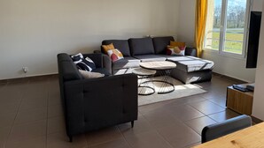 A modern living room with a sectional sofa, a small round table, and a TV stand.