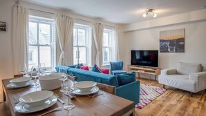 Ein modernes Wohnzimmer mit einem Holzespeisetisch, der für eine Mahlzeit gedeckt ist, einem blauen Sofa, einem weißen Sessel und einem Flachbildfernseher.