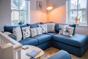 Ein gemütliches Wohnzimmer mit einem blauen Ecksofa, einem kleinen runden Holztisch und einer Stehlampe.