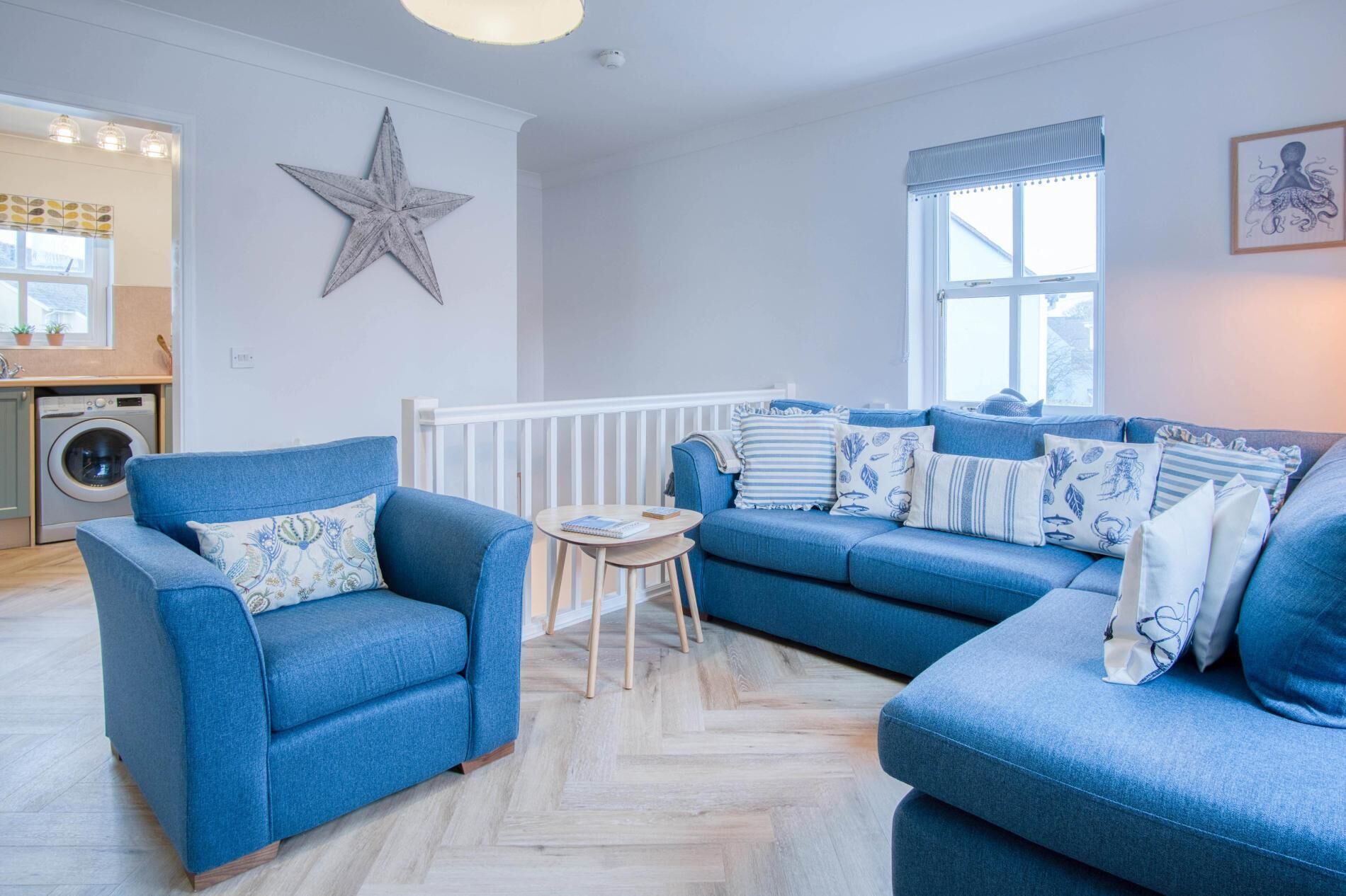 A living room with a blue sofa set, a star decoration on the wall, and a window with curtains.