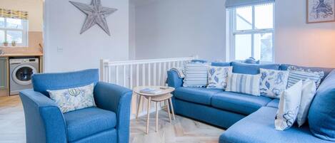 A living room with a blue sofa set, a star decoration on the wall, and a window with curtains.