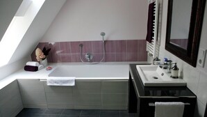 Ein modernes Badezimmer mit freistehender Badewanne, einem Waschtisch mit Spiegel und einem Fenster, das für natürliches Licht sorgt.