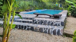 A swimming pool with stone steps, surrounded by lush greenery and a fence. - The Cozy Acorn Resort (Nainital)