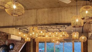 A restaurant interior with brick walls, large windows, and multiple hanging wicker chandeliers. - The Cozy Acorn Resort (Nainital)
