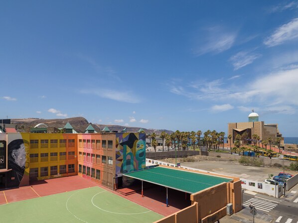 A basketball court adjacent to colorful buildings with a view of the sea and mountains. - CITY FAMILY AUDITORIUM (Las Palmas de Gran Canaria)