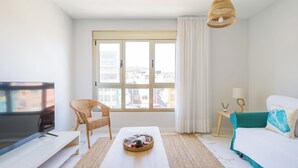 A modern hotel room with a large window, a television, a wicker chair, a wooden table with a basket, a teal bed, and a hanging light fixture. - CITY FAMILY AUDITORIUM (Las Palmas de Gran Canaria)