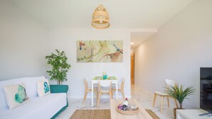 A modern living room with a white sofa, a dining table with chairs, a TV, and a painting on the wall. - CITY FAMILY AUDITORIUM (Las Palmas de Gran Canaria)