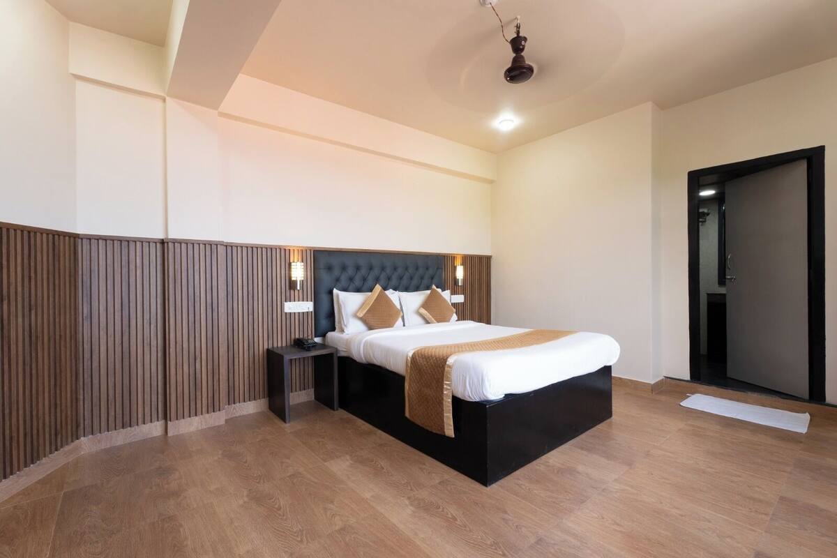 Quarto de hotel moderno com uma cama grande, uma parede de destaque em madeira, uma mesa de cabeceira e uma luminária no teto.