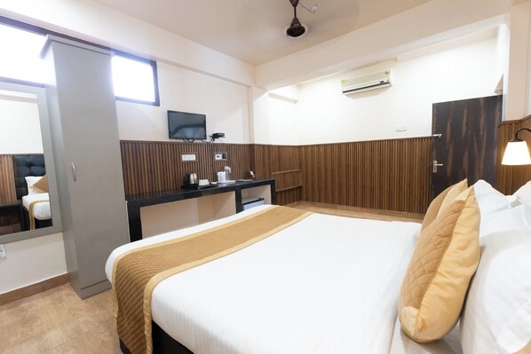 A hotel room with a bed, a desk, a television, and an air conditioning unit.