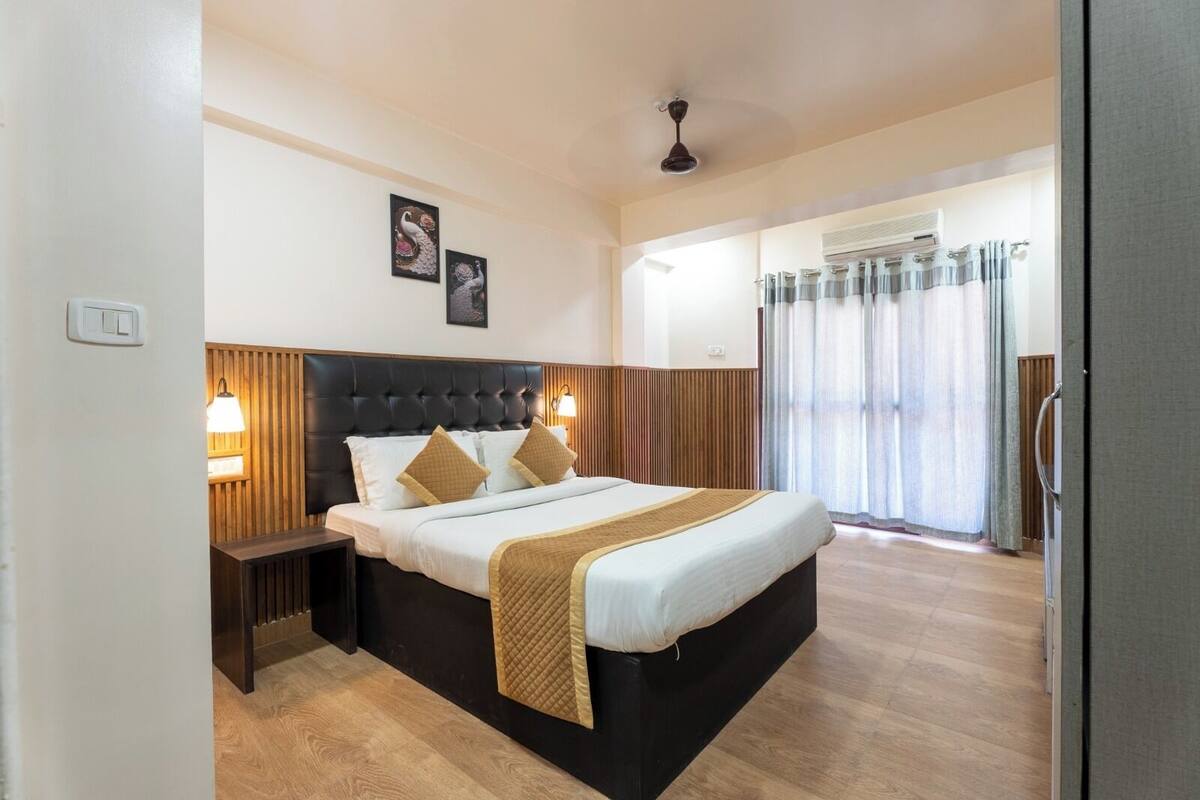 Quarto de hotel com uma cama grande, painéis de madeira nas paredes, um ventilador de teto e uma janela com cortinas.