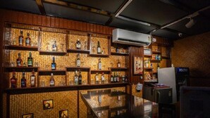 A bar area with shelves of liquor bottles, a polished bar counter, and a refrigerator. - Hotel Mainak & Health Club (Port Blair)