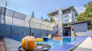 A swimming pool area with a glass enclosure, a lounge chair, and a tray with drinks and a fruit. - Hotel Mainak & Health Club (Port Blair)