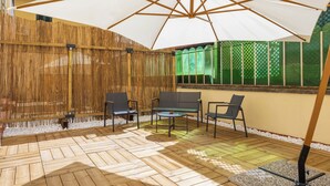 Un patio al aire libre con piso de madera, un paraguas grande de color blanco y varias sillas.