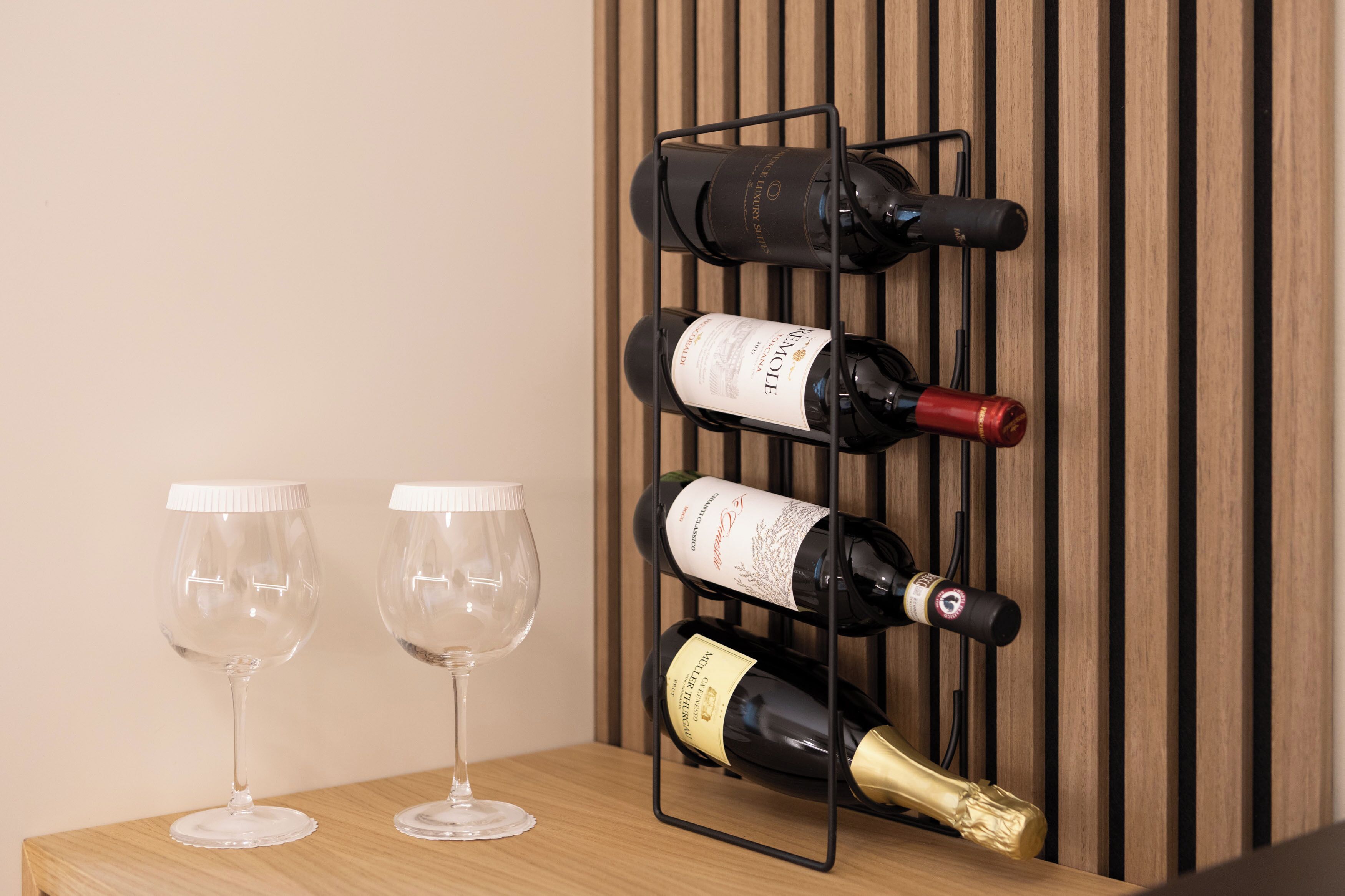 A wine rack with bottles and two empty wine glasses on a wooden surface.