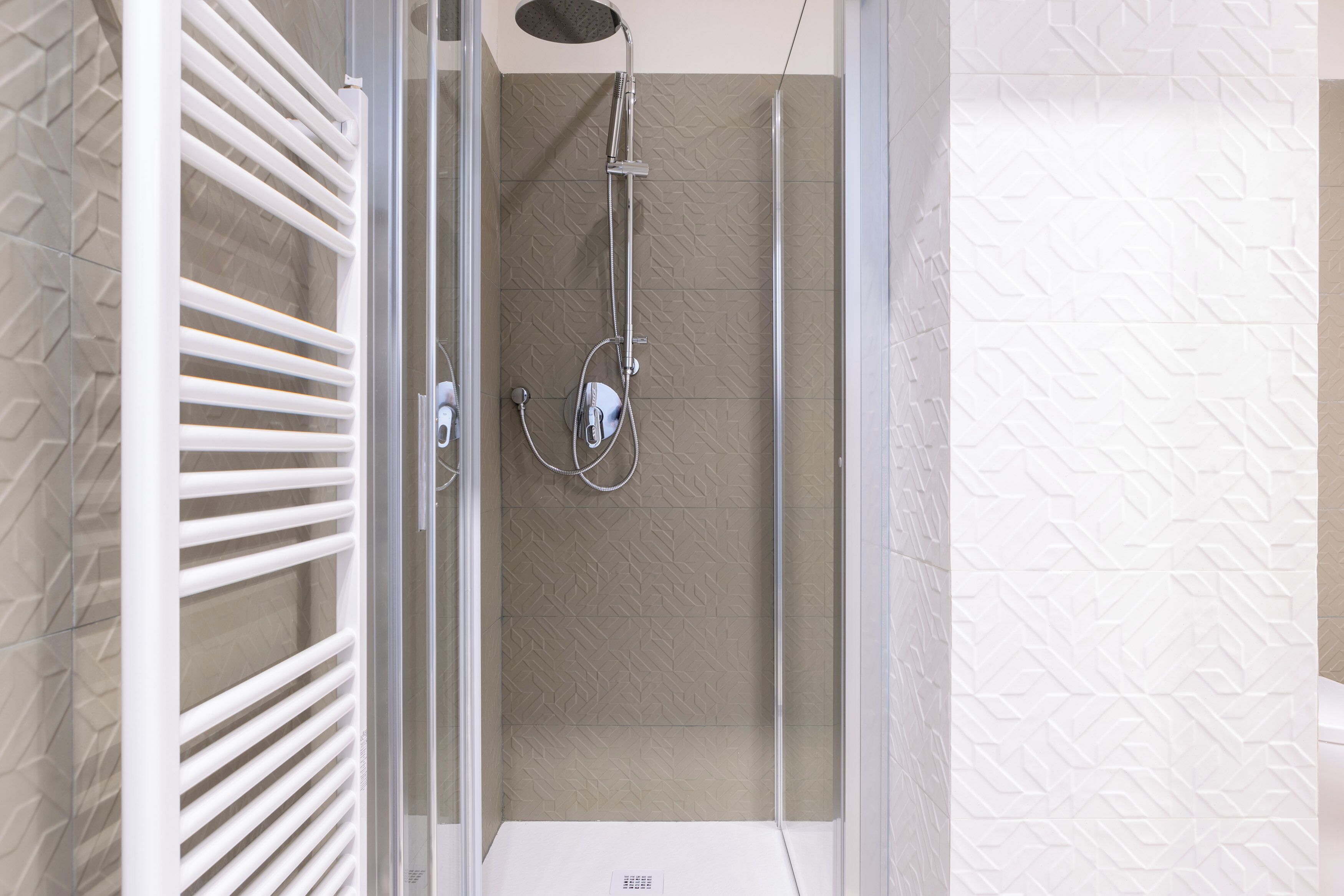 A modern shower with a glass door, a handheld showerhead, and a wall-mounted control panel.