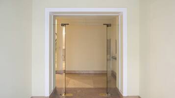 A hallway with a glass door leading to another room. The walls are painted in a light color, and the floor is tiled.